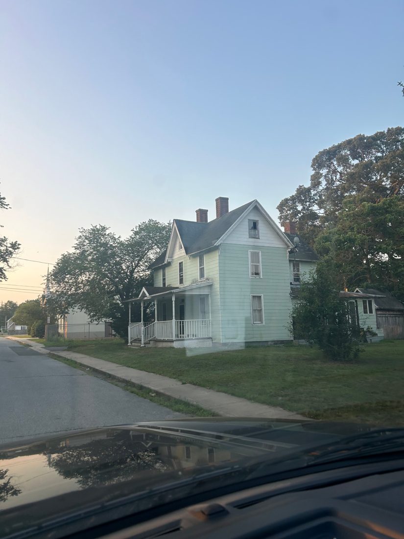 An old two-story house with a front porch and outbuilding on a town corner lot