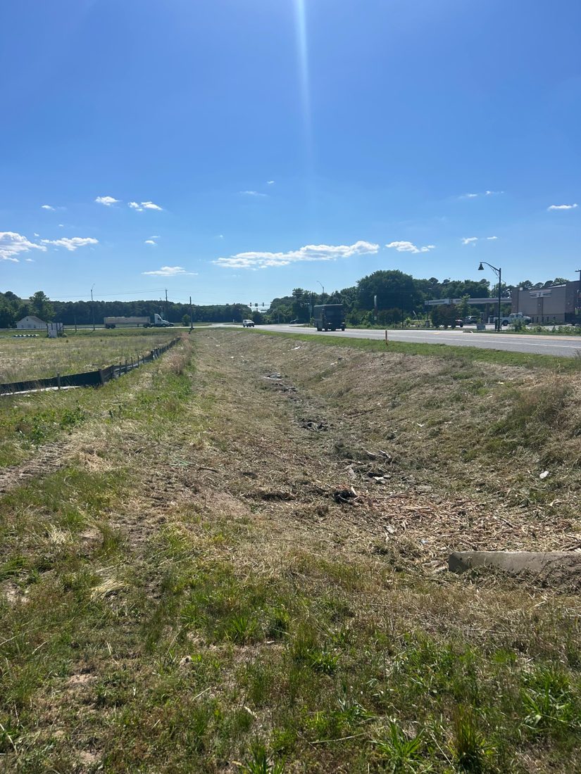 The same roadside ditch cleared down to grass and mulch, open and draining along the highway