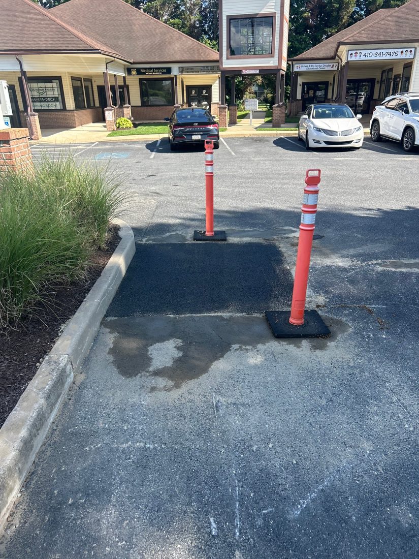 The same parking lot section backfilled and patched with fresh asphalt, marked off with safety delineators